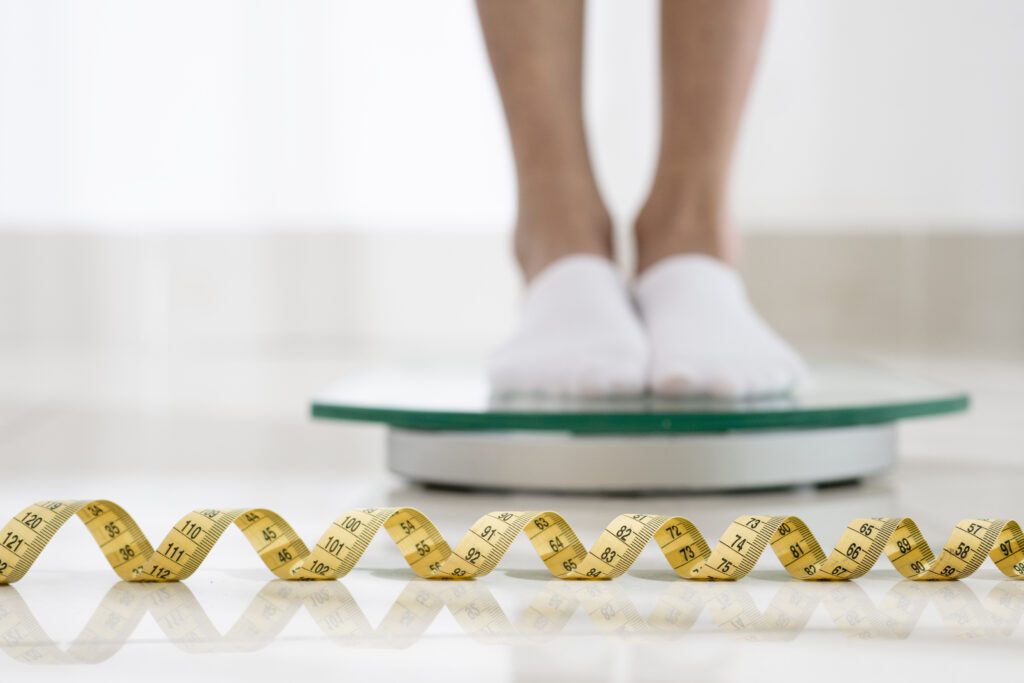 A woman standing on a weighing scale with a measuring tape in front of her 